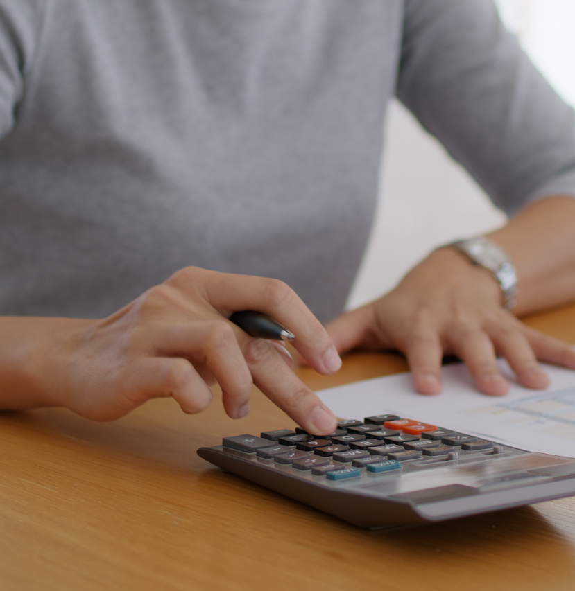 A person wearing a gray shirt uses a calculator while holding a pen, with papers on a wooden desk, meticulously financing a total solution.