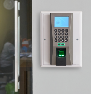 A biometric fingerprint scanner with a keypad, part of advanced access control systems, is installed on a wall near a glass door.