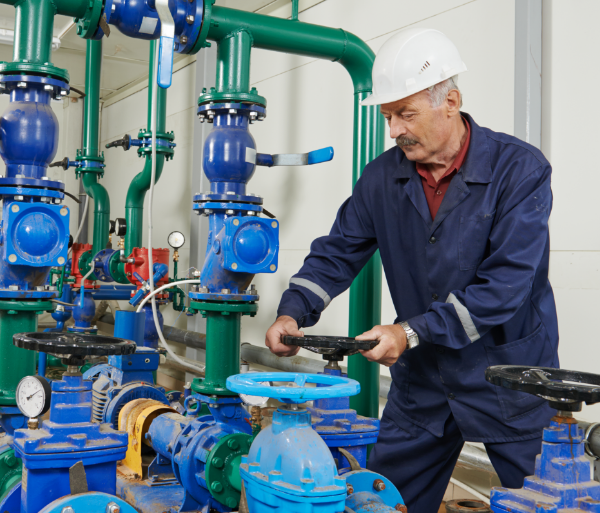 A worker in protective gear and a white hard hat adjusts a valve on a blue industrial piping system connected to the facility's fire pumps.